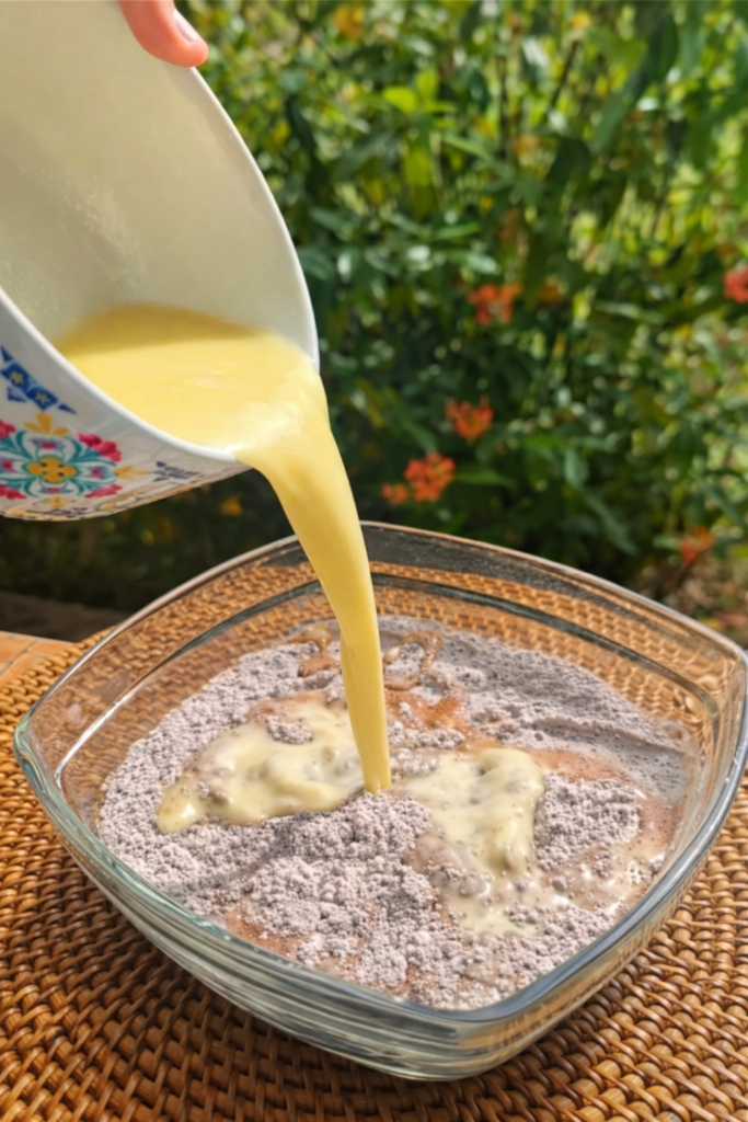 Dodavanje tečnih sastojaka u suhe sastojke tokom pripreme čokoladnog mochi kolača.