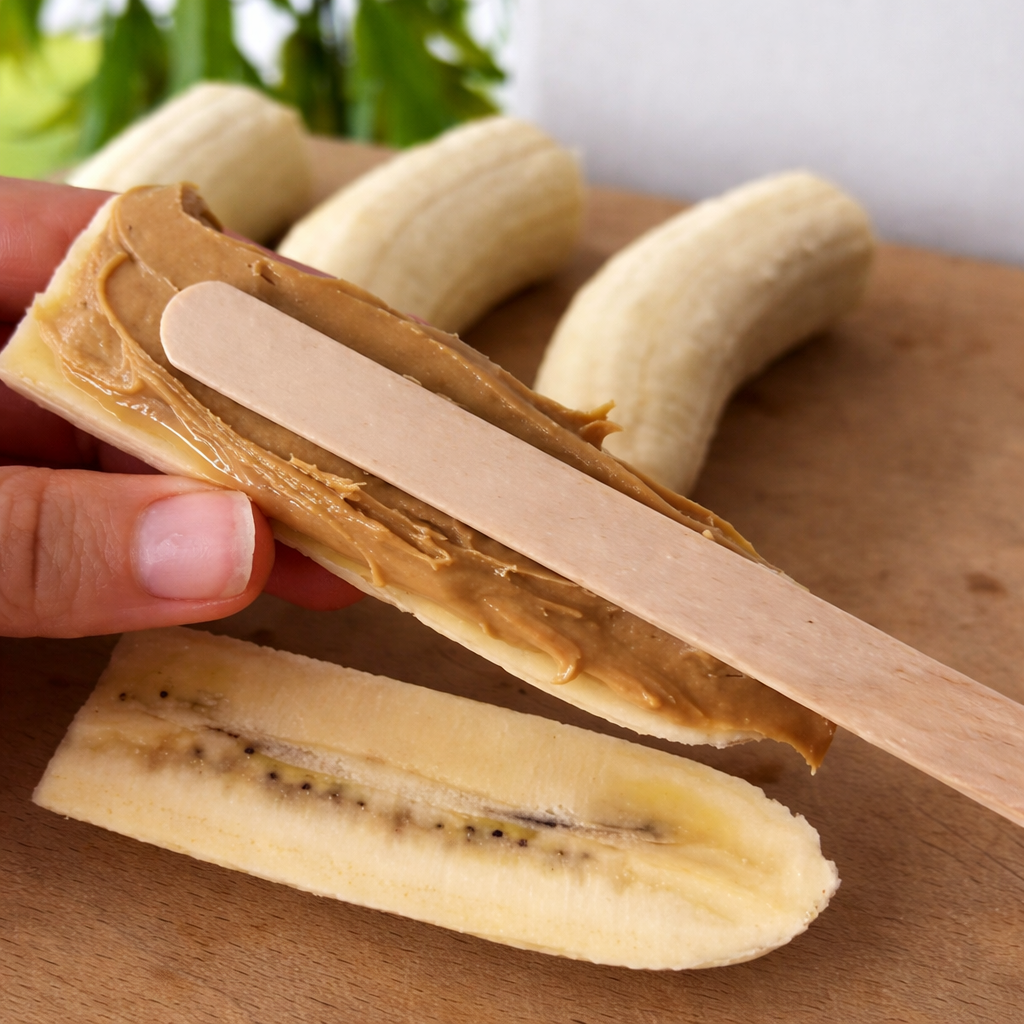Banana prerezana po dužini premazana kikiriki puterom sa drvenim štapićem u sredini