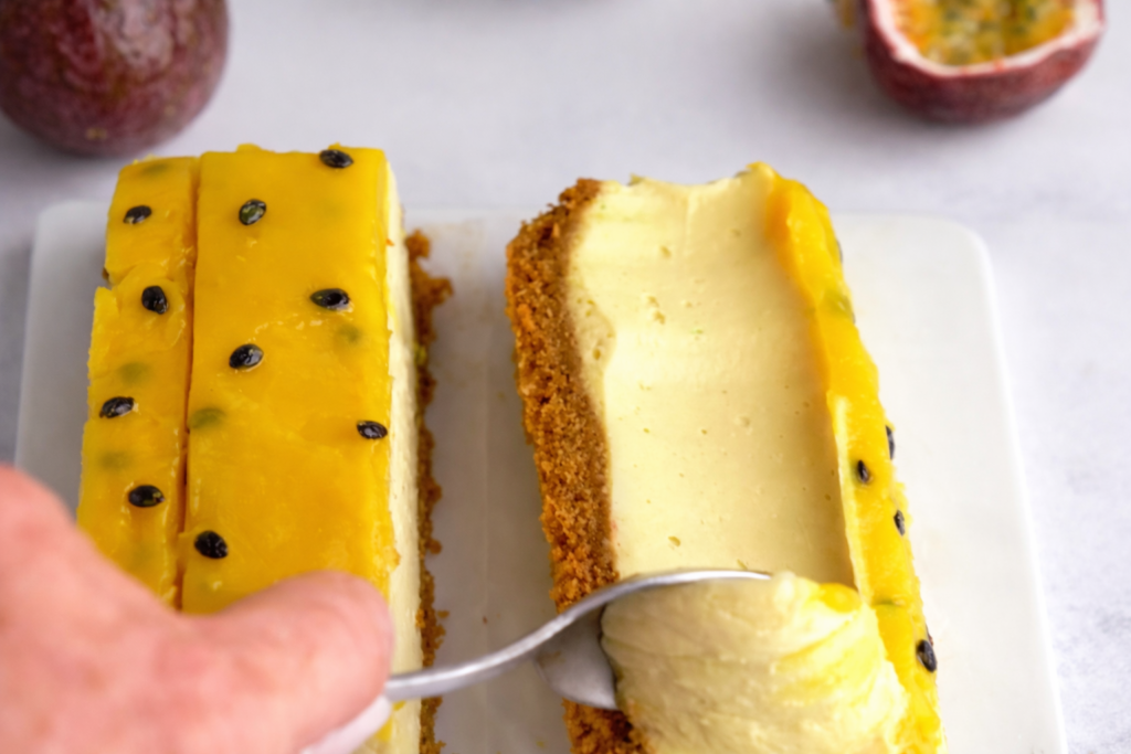 Kremasti presjek cheesecakea sa marakujom na podlozi od keksa sa žutim voćnim prelivom