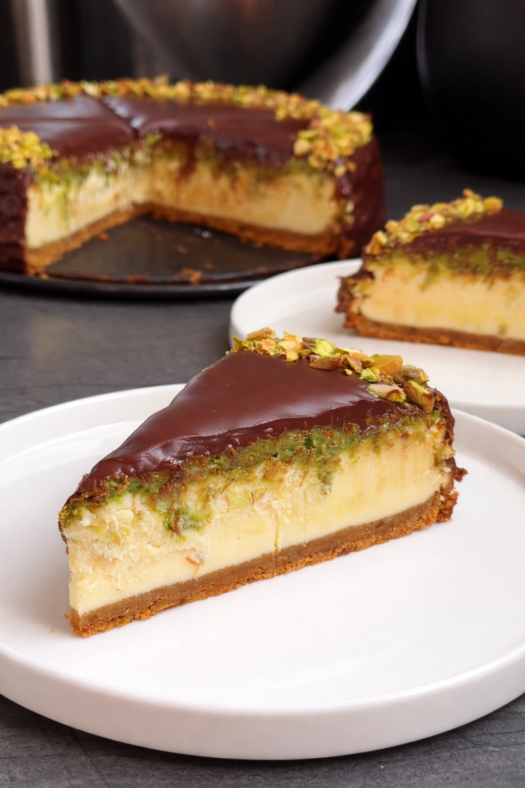 Dubai style cheesecake sa sirom i pistaćima preliven čokoladom, kremasti presjek domaćeg kolača na bijelom tanjiru