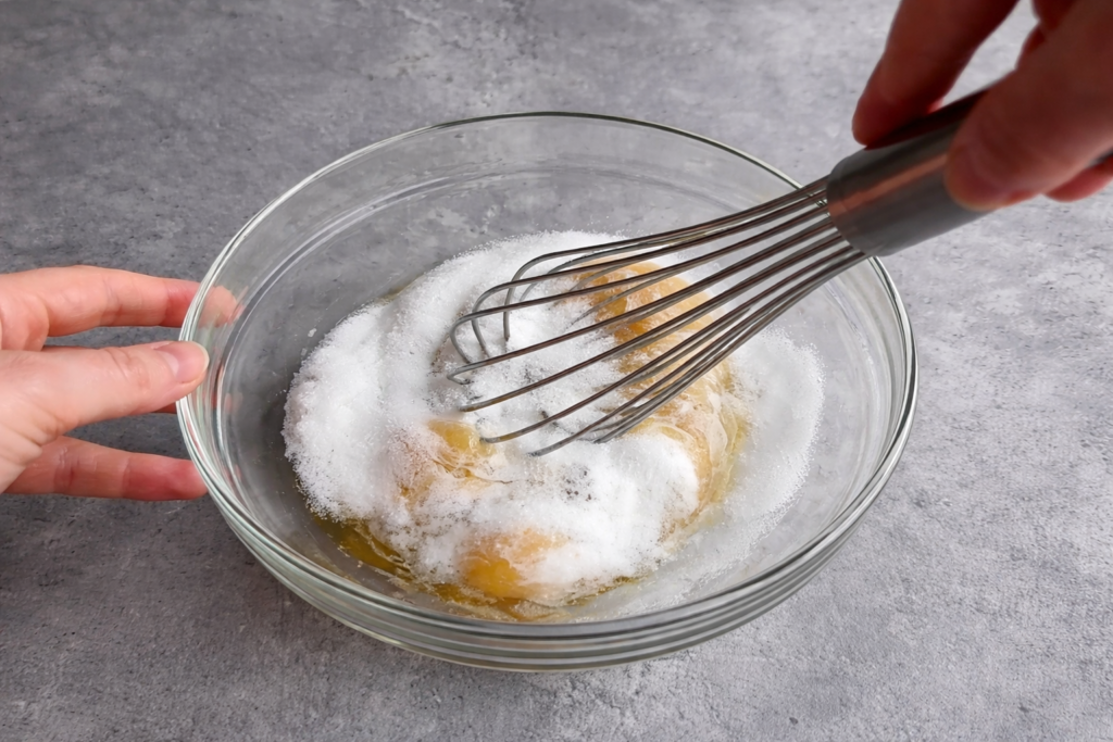 Ručno mućenje maslaca, šećera i jaja pjenjačom u staklenoj zdjeli