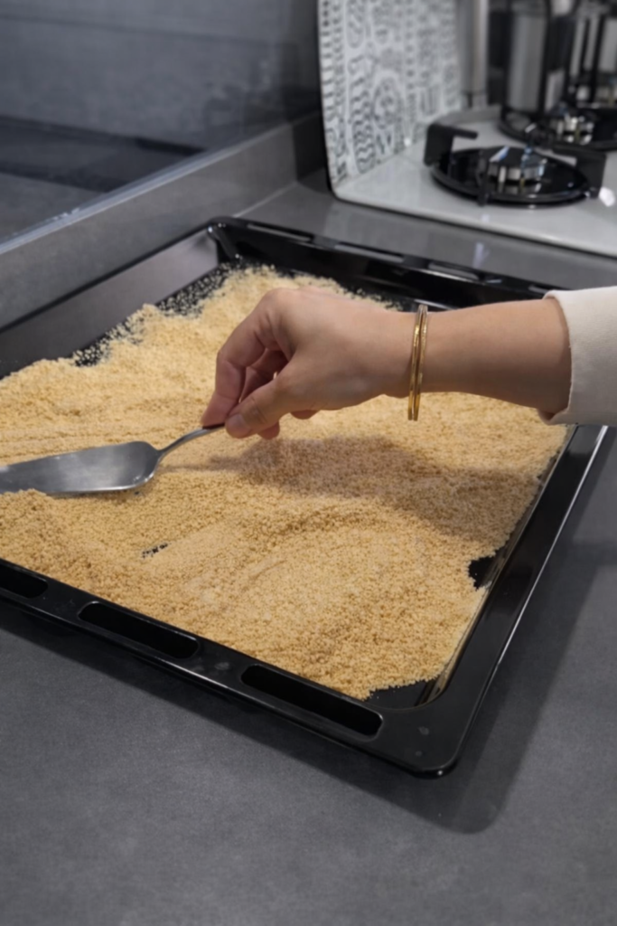 Poravnavanje podloge od mljevenog keksa u plehu kao prvi korak pripreme Sultan paša kolača