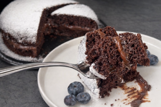 Sočni čokoladni kolač sa krem sirom i čokoladnim filom, presjek parčeta posut šećerom u prahu