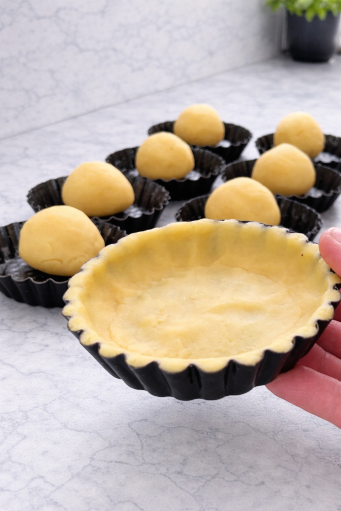 Oblikovanje prhkog tijesta u male kalupe za korpice prije pečenja domaćih voćnih tartova