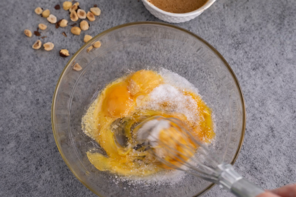 Žumanca i šećer u staklenoj posudi tokom mućenja za tiramisu kolač