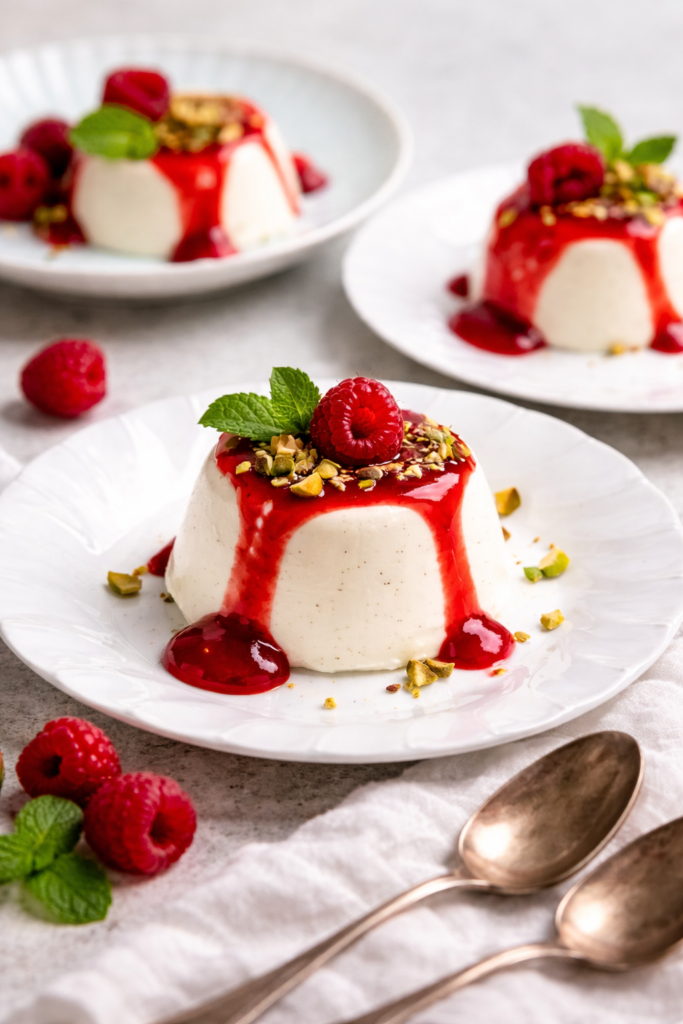 Panna cotta sa preljevom od malina, pistacijama i svježim malinama na bijelom tanjiru