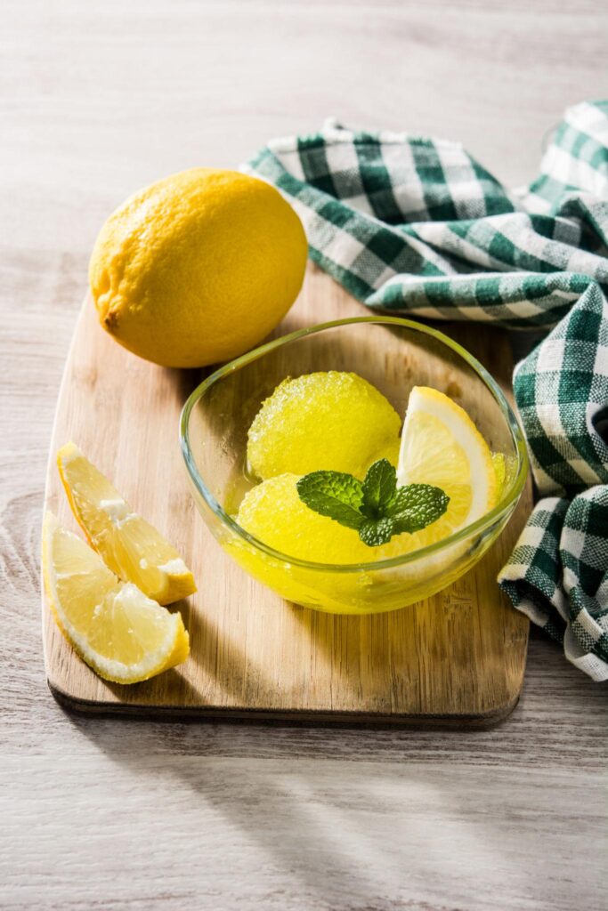 Domaći sorbet od limuna poslužen u staklenoj zdjelici sa svježim listićima mente i kriškom limuna.