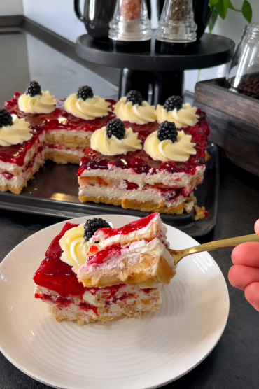 Kremasta torta od vafela sa mascarpone kremom i preljevom od šumskog voća, ukrašena kupinama i ružicama od šlaga.