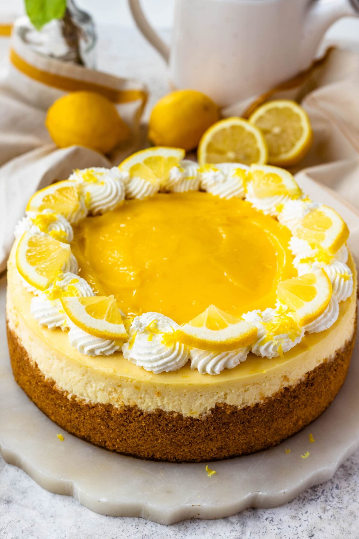Kremasti limunov cheesecake ukrašen šlagom, lemon curdom, kriškama limuna i naribanom limunovom koricom.