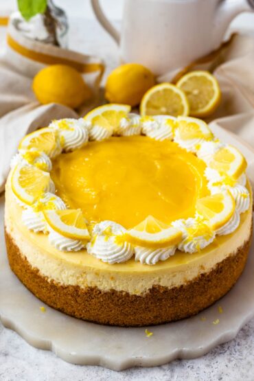 Kremasti limunov cheesecake ukrašen šlagom, lemon curdom, kriškama limuna i naribanom limunovom koricom.