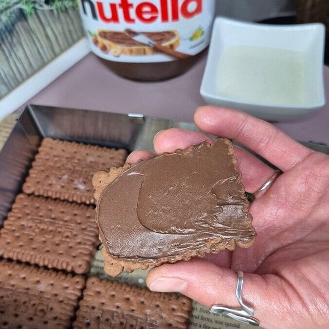 Premazivanje kakao keksa Nutellom prije slaganja tiramisua bez pečenja.