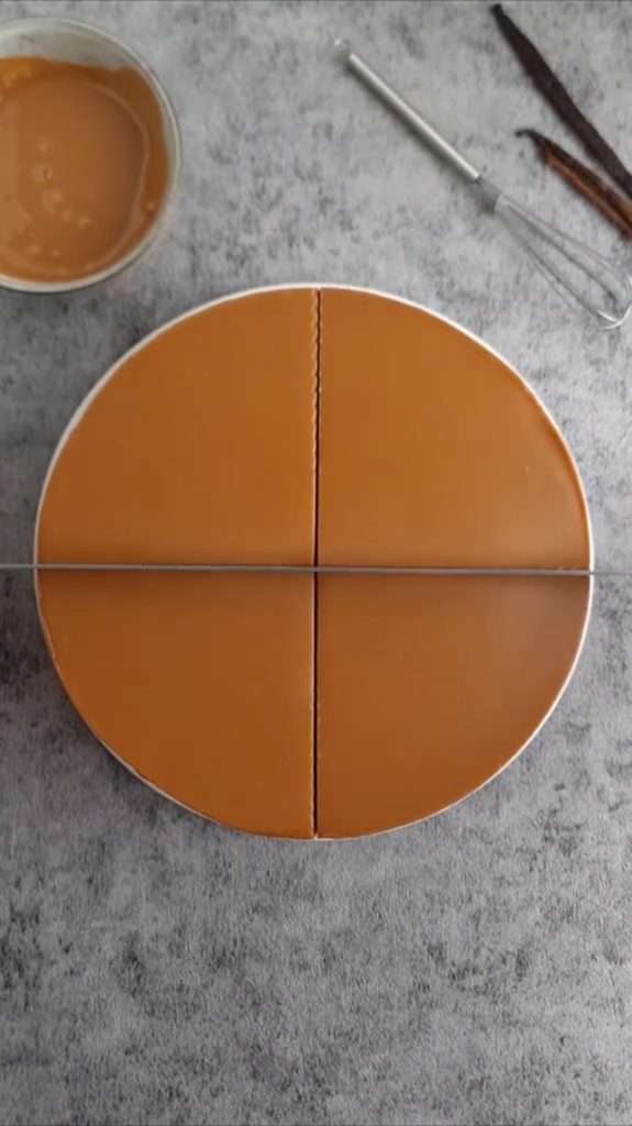 Torta s glatkim smeđim preljevom na bijelom tanjiru, prikazana odozgo tokom rezanja