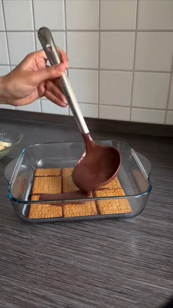 Topla kakao krema sipa se preko prvog reda petit keksa u staklenoj tepsiji