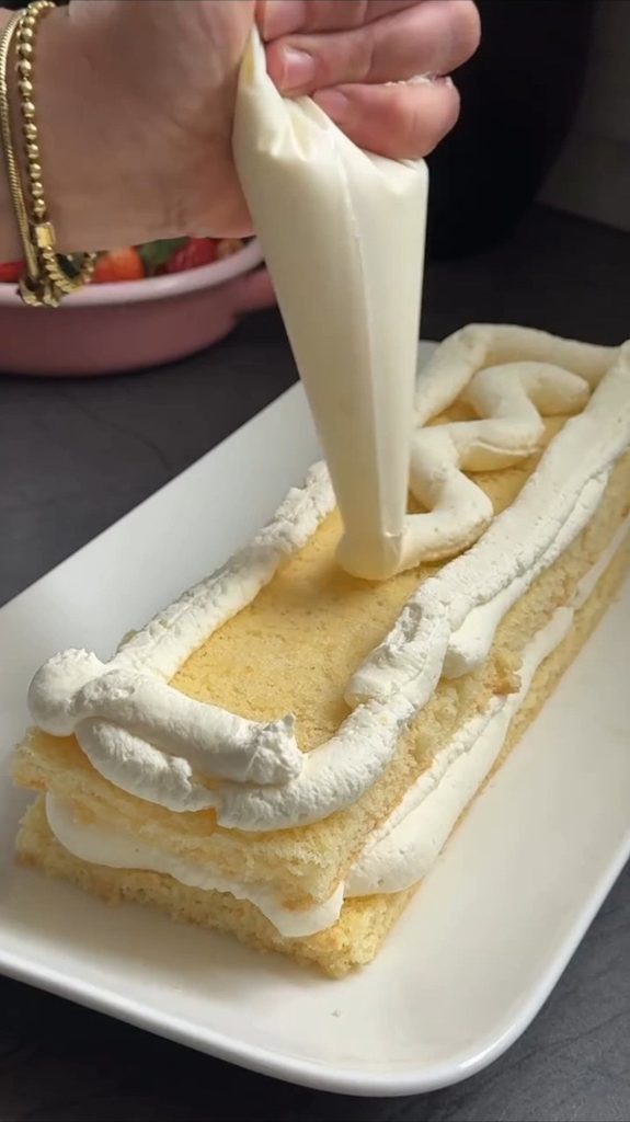 Nanošenje bijele kreme slastičarskom vrećicom na pravougaoni sloj biskvita