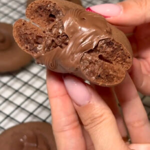 Ruke drže prelomljeni čokoladni keks s Nutellom na površini