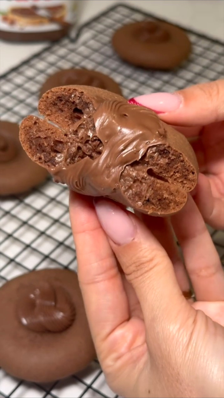 Ruke drže prelomljeni čokoladni keks s Nutellom na površini