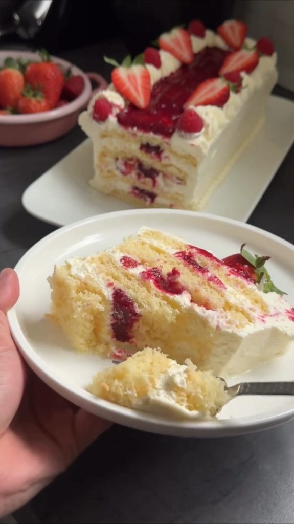 Komad torte s biskvitom, bijelom kremom i crvenim voćnim nadjevom na bijelom tanjiru